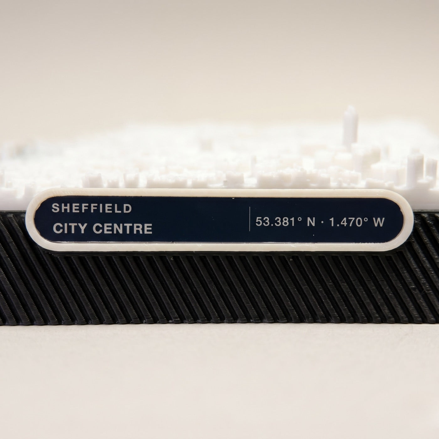 Macro close-up of the engraved label reading SHEFFIELD CITY CENTRE 53.381 degrees N 1.470 degrees W on the ribbed black base.